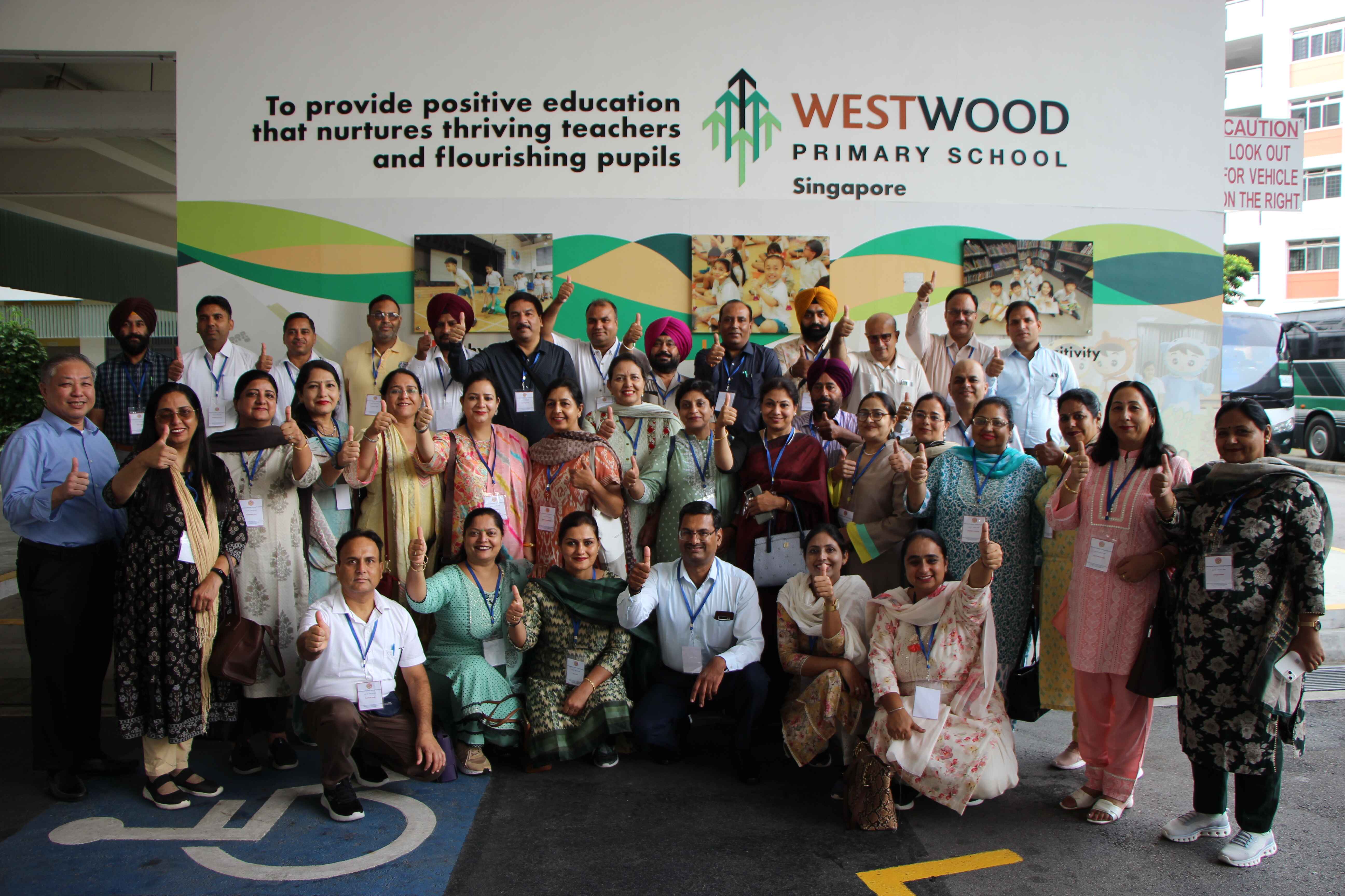 Large group of adults giving thumbs up in front of Westwood Primary School Singapore wall mural.